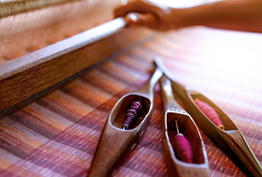 Woman working on weaving machine for weave handmade fabric. Textile weaving. Weaving using traditional hand weaving loom on cotton strands. Textile or cloth production in Thailand. Asian culture.