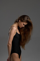 Fototapeta premium Woman with long hair in black bodysuit looking down, posing against gray background with soft lighting.