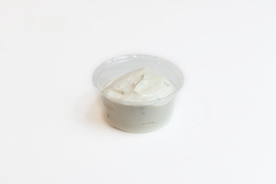 Small cup of ranch dressing with pieces of herbs placed on a plain background