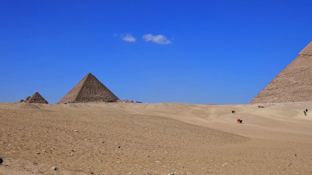 Giza pyramids, desert plateau, Egypt. Iconic ancient wonder under vivid blue sky. Travel and history. Pan shot.