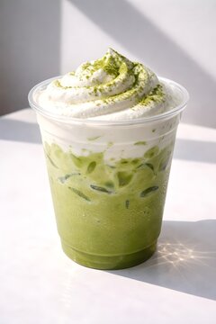 Iced Creamy Matcha Latte with Whipped Cream. photograph of an iced creamy matcha latte topped with soft whipped cream and matcha powder, served in a transparent plastic cup.