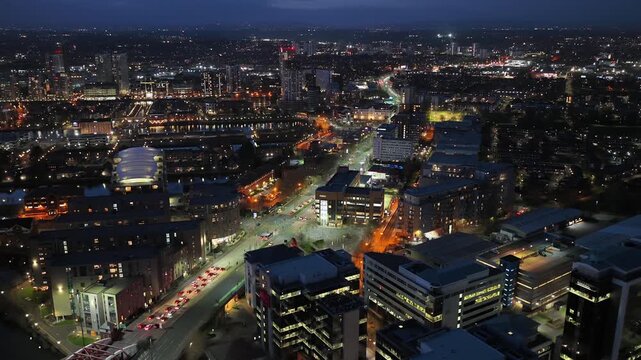 Aerial video of the illuminated Salford Quays waterfront, the River Irwell, and the distant Manchester city skyline at night, UK.