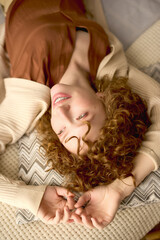 Obraz premium Curly young woman relaxing in her modern beige apartment with a joyful smile
