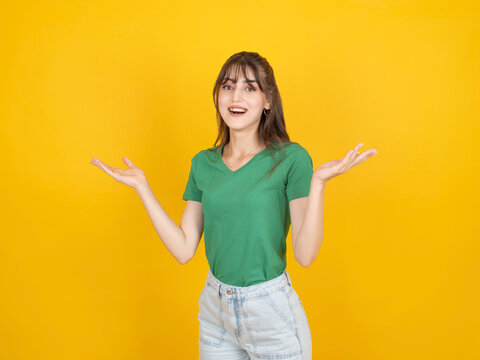 Confused caucasian woman raising hands with unsure expression, questioning situation or not understanding, wearing green t shirt and denim, isolated on yellow studio background with copy space.