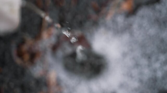 Extreme close-up of rainwater stream flowing from a house drain pipe. Clear water pouring from a roof gutter downspout with strong selective focus, highlighting the flowing stream while the background