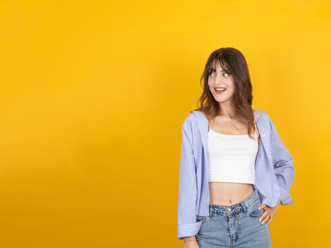 Smiling caucasian woman looking aside with cheerful expression, wearing striped shirt and denim, standing isolated on bright yellow studio background with wide copy space. Online offer concept idea.