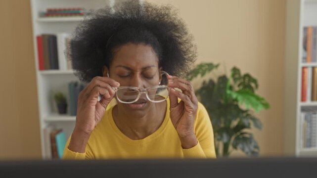 Woman touches temple at a computer screen in a building, hand pressed to forehead and eyes closed in tense posture; stress headache.