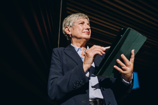 Close-up of senior woman&rsquo;s hands using stylus on blank tablet screen, emphasizing precision, mobility, and digital control in a tech-savvy professional environment.
