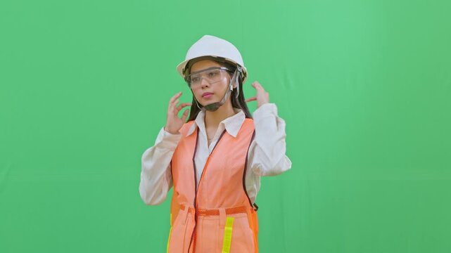 A female engineer adjusting her hair to fit properly under her white safety helmet. Emphasizing grooming and PPE compliance on a green screen.