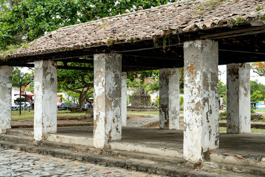 A wide view of the weathered stone pillars and clay tile roof of the historic old fish market pavilion in Paraty, Brazil.