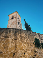 Old white church tower behind a stone wall under a clear blue sky. Colmenar, Malaga, Andalusia, Spain.