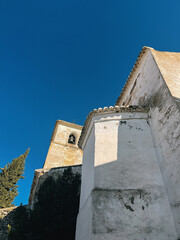 Old white church with pine tree under a clear blue sky. Colmenar, Malaga, Andalusia, Spain.