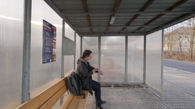 Man sitting on bench at bus stop checking time before leaving.
Urban scene capturing waiting and departure moment.
