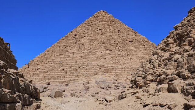 Close-up view of Pyramid of Menkaure with subsidiary pyramids and ancient stone ruins at Giza, Egypt. Massive limestone blocks against vivid blue sky. Travel and history.