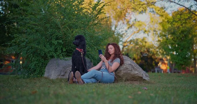 A young woman tosses her phone aside in the park and gives her dog her full attention, capturing presence, affection, and an undistracted moment outdoors.