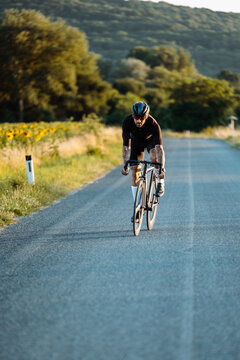 Solo Male Cyclist Moving Forward On Peaceful Country Road Decorated With Blooming Sunflowers