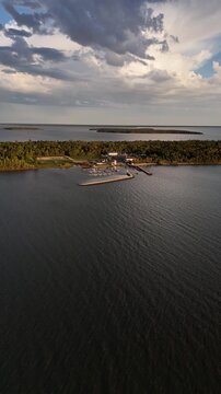 Drone flying forward toward Gull Harbour on Hecla Island Manitoba. Vertical aerial view showing marina, breakwall, boats, island, and shoreline of Lake Winnipeg on a sunny summer day.