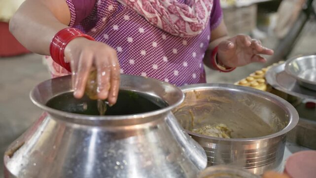 Closeup shot of female vendor's hands preparing panipuri or fuchka using hands without gloves and ingredients in metal pots. Street food preparation and everyday market life in India South Asia