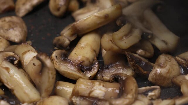 Close-up of sliced mushrooms frying in a pan as a chef stirs them with a wooden spatula, showing sizzling texture and appetizing cooking action