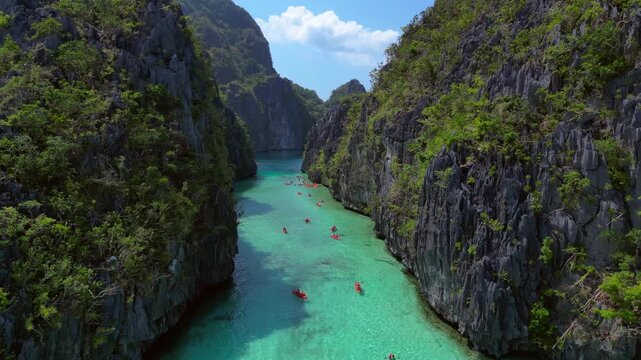 Clear turquoise water and towering limestone karsts surround kayakers paddling through Big Lagoon, a popular tourism destination. speed ramp, time lapse. Fantastic aerial view fly push forward panora