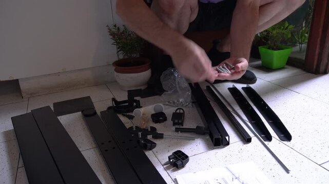 Person working on assembling furniture indoors with visible hardware pieces and tools on the floor.