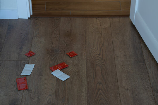condoms packs scattered on a dark wooden floor in a room with white walls
