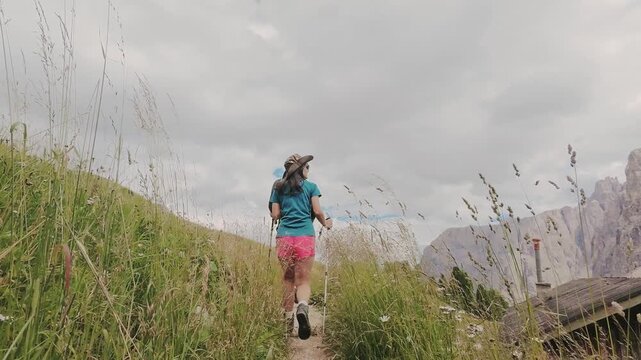 Aerial pov couple hikes together along rugged trail toward the jagged Rossz&auml;hne peaks in the Italian Dolomites. Majestic limestone peaks. UNESCO World Heritage scene. Gardena pass lope hiking trail