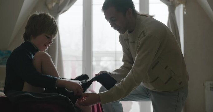 Man puts warm clothes on child. Dad help child to dress at home. 4K 10-bit