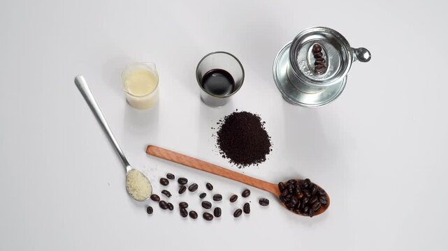 Top-down rotating flat lay of a full Vietnamese coffee combo: sugar, beans, ground coffee, milk, and phin filter on a white background. Professional recipe concept.