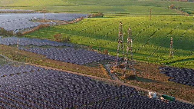 Aerial drone view of a massive solar panel farm in golden hour light, renewable energy infrastructure for the UK grid upgrade at Tye Lane.