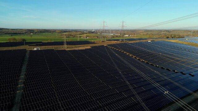 Aerial drone view of a massive solar panel farm in golden hour light, renewable energy infrastructure for the UK grid upgrade at Tye Lane.