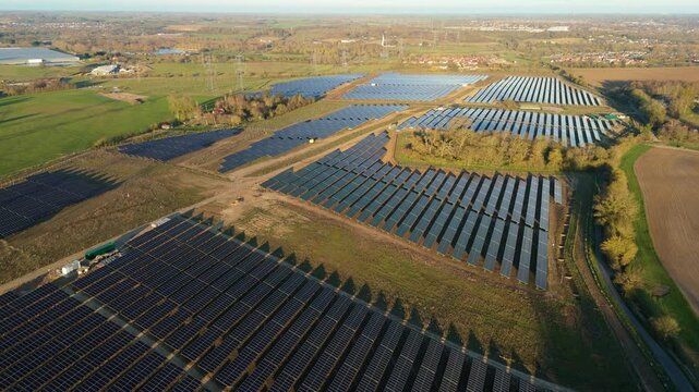 Aerial drone view of a massive solar panel farm in golden hour light, renewable energy infrastructure for the UK grid upgrade at Tye Lane.