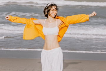 Young woman stretching arms with headphones on sandy beach shoreline