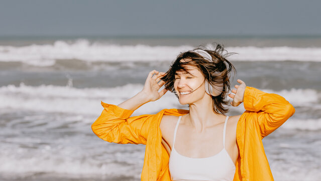 Young woman smiling with headphones on sandy beach shoreline