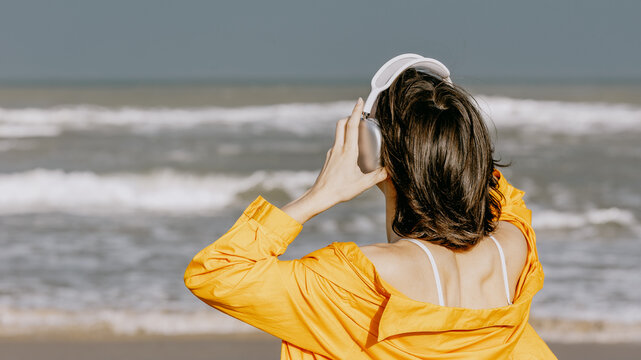 Woman wearing headphones facing ocean waves on shore