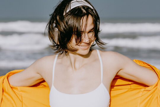 Young woman adjusting jacket and smiling at ocean beach