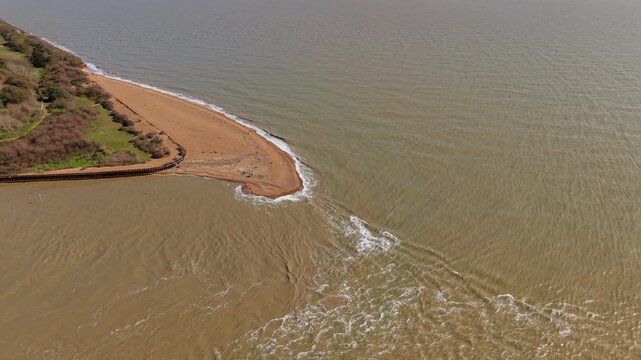 Top down aerial view of sand bank and tidal flow in a British estuary during ebb tide with waves rushing in.