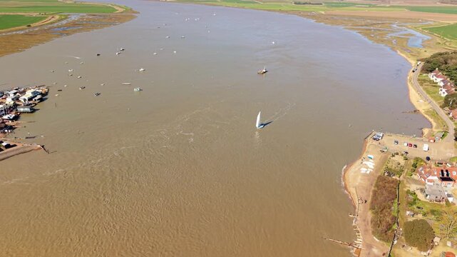 Aerial drone view of a small yacht sailing against the tide in the Deben Estuary, Felixstowe Ferry, UK