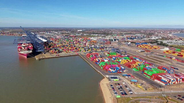 Aerial drone perspective of global maritime trade showing a large cargo vessel taking on freight at Felixstowe container terminal, England