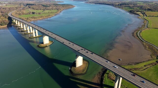 Aerial view of the massive Orwell Bridge spanning the River Orwell estuary near Ipswich, traffic crossing a concrete road bridge over blue water on a sunny day in Suffolk, UK.