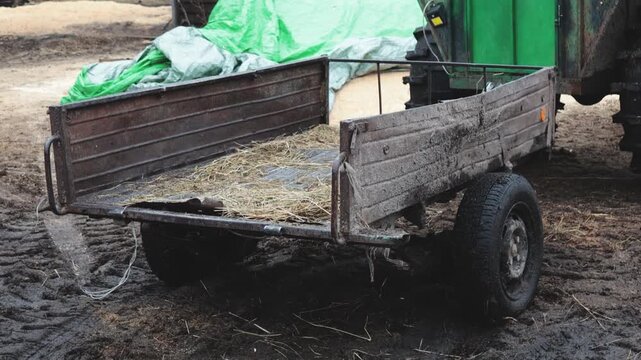 A green tractor pulls a trailer loaded with hay on a rural road