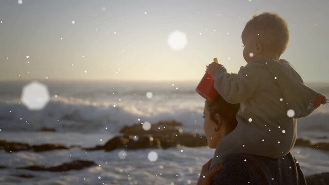 Parent holding child on shoulders at shore, raising red bucket peering at sunset, bokeh drifting