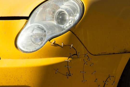 Close-up of a Cracked Yellow Car Bumper Repaired with Plastic Zip Ties