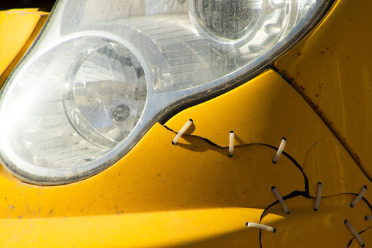 Close-up of a Cracked Yellow Car Bumper Repaired with Plastic Zip Ties