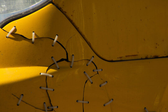 Close-up of a Cracked Yellow Car Bumper Repaired with Plastic Zip Ties