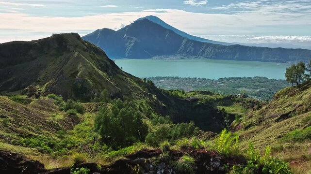 Man training parkour running on a mountain cliff top overlooking Batur Lake and Mount Batur volcano, representing strength, determination, and connection with nature in an impressive outdoor landscape