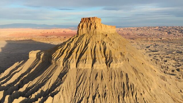 Aerial view of Factory Butte showing unique erosion patterns and desert badlands under a soft sky in Wayne County, Utah, United States.