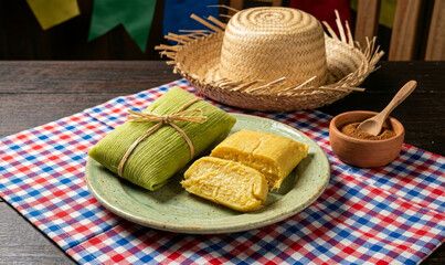 Pamonha brasileira tradicional em prato rústico com chapéu de palha e decoração de Festa Junina sobre mesa de madeira