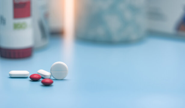Round white tablets and blurred red and white tablets pills. Pills on blurred pills plastic bottle. Healthcare and pharmaceutical industry. Pharmacy or polypharmacy concept. Prescription drugs.