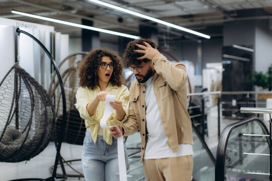 Surprised couple reacting to high shopping prices on long receipt